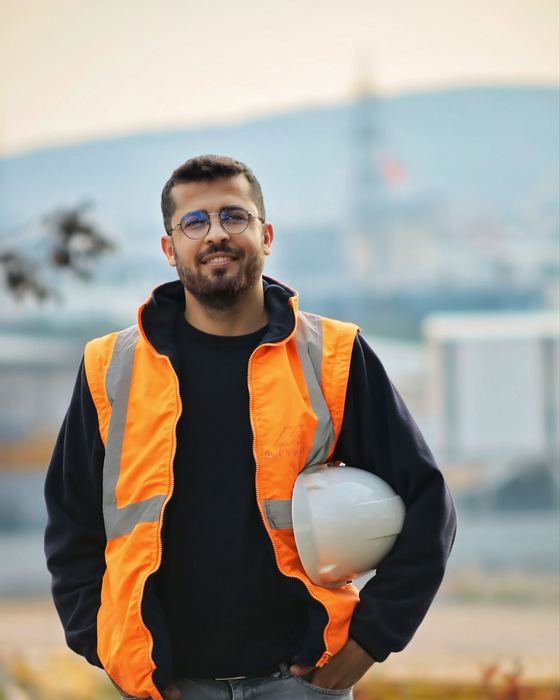 איש מקצוע צעיר באפוד זוהר, מחזיק קסדת מגן ומחייך